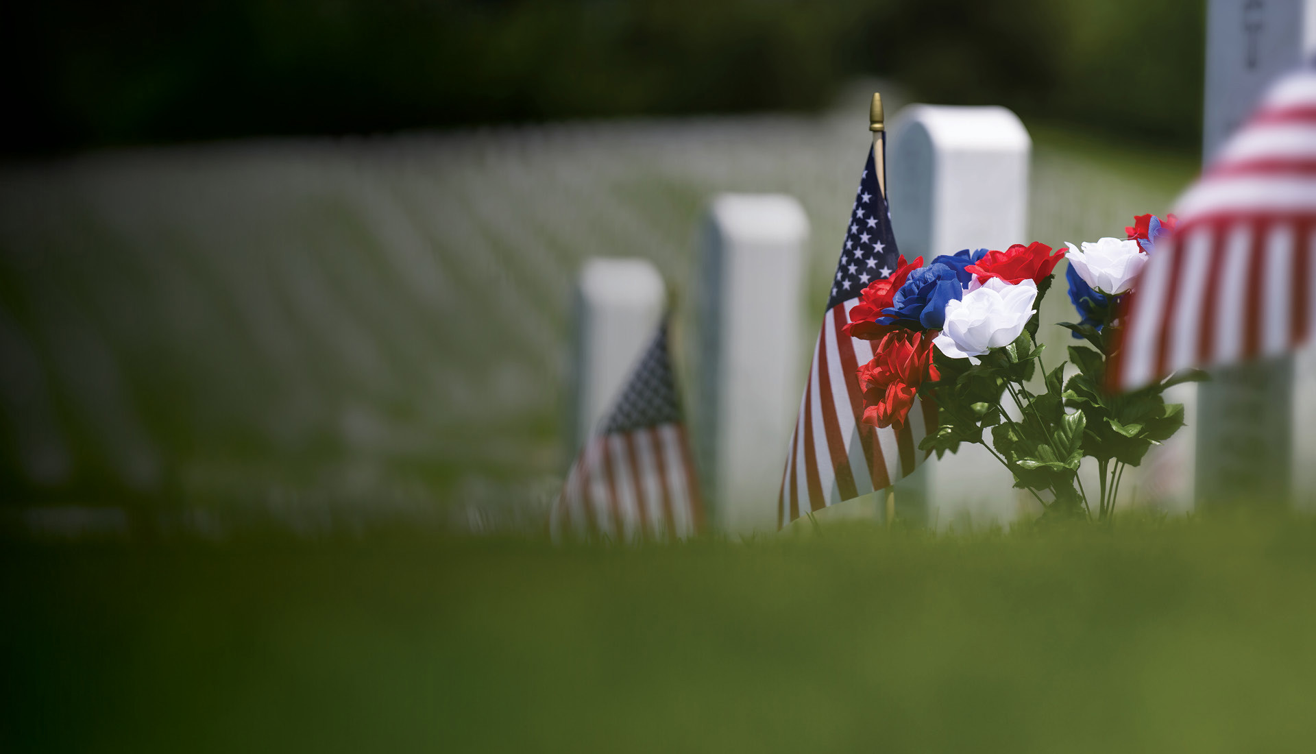 A Memorial Day picture of US flags and flowers by a gravestone at a military cemetery.