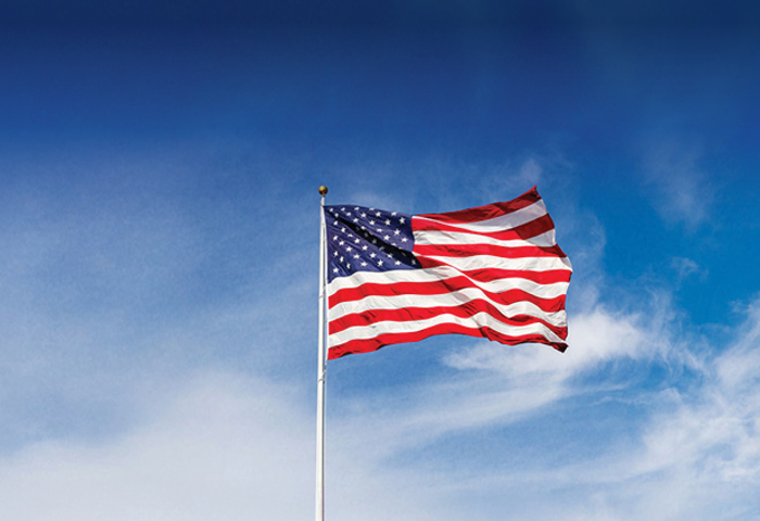 American flag waving on a flagpole against a bright blue sky with wispy clouds on a sunny day.