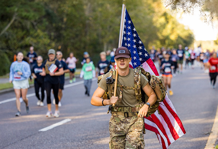 Carry Forward participant walking with an American flag with fellow participants on the route behind him.