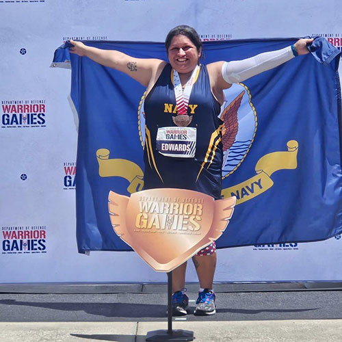 Navy veteran Maria Edwards holding a Navy flag after being presented the bronze medal at the 2024 DoD Warrior Games.