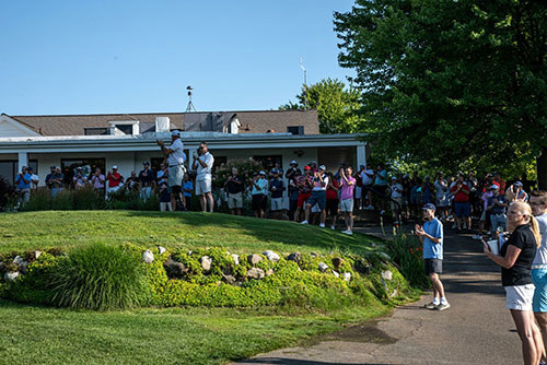 Group of people standing on a golf course green, many of them clapping