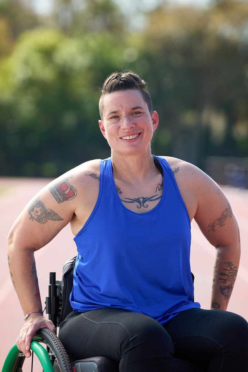 Beth King, veterana herida, en una silla de ruedas y sonriendo con una pista de fondo.