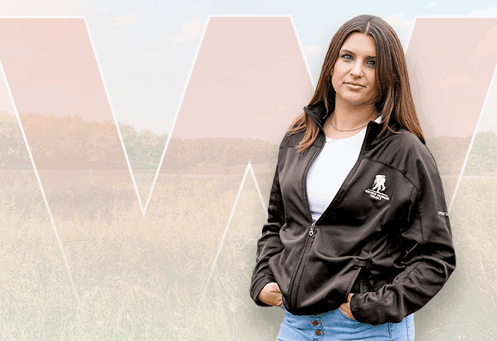 Wounded warrior Keara Torkelson smiling in a field while wearing a black WWP jacket with her hands in the pockets.