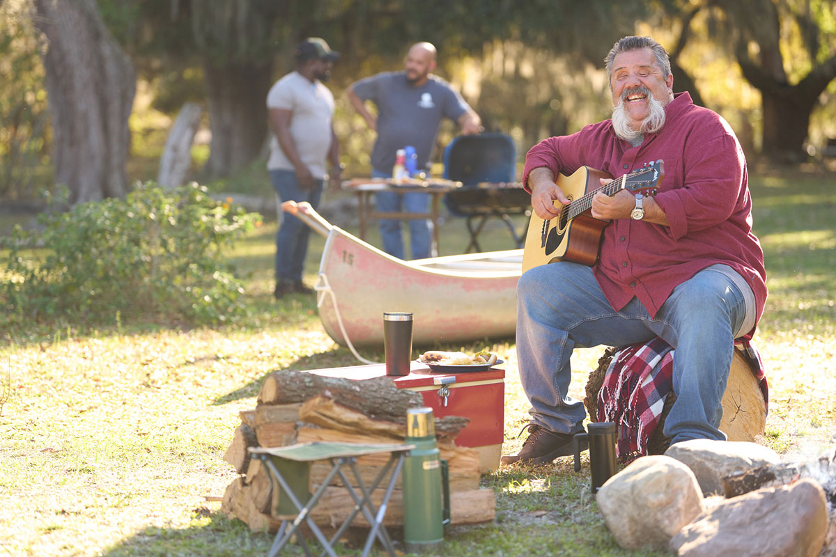 Wounded warrior Aaron Cornelius playing the guitar around a fire during an outdoor event.