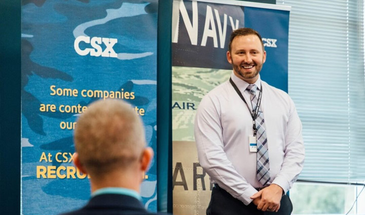 A male CSX employee smiles as he stands in the front of a meeting room during a job fair.