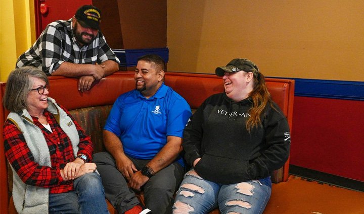 Wounded Warrior Tim Aponte sitting inside while smiling and talking with three fellow warriors.