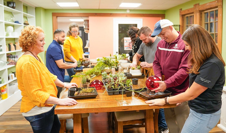 Los veteranos heridos Dawn Bonebrake, Nathan Covey, Laura Jennings, Camella Andrews, Chris Kallas, Brent Whitten y Keara Torkelson están alrededor de una mesa, sonriendo, en un taller de cultivo de plantas.