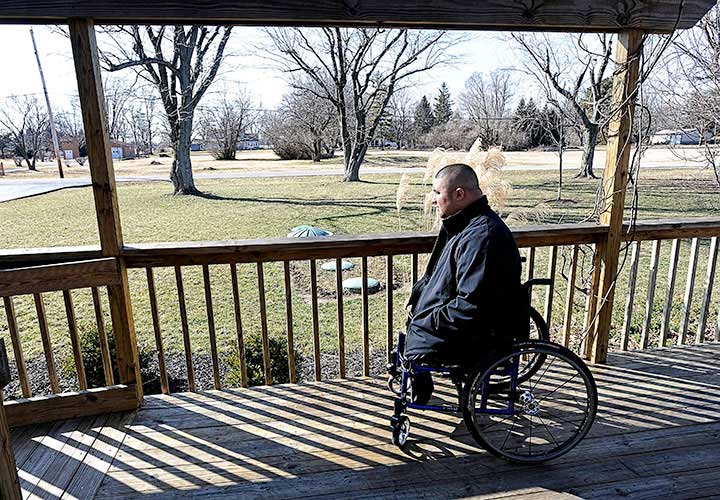 Wounded warrior Shane Parsons sits in his wheelchair on the front porch while wearing a winter coat.