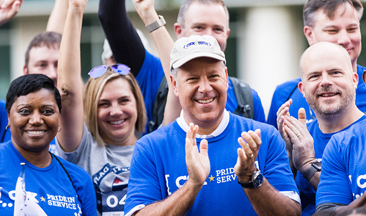 CSX employees wearing blue company t-shirts clap and cheer outdoors at a WWP Carry Forward event.