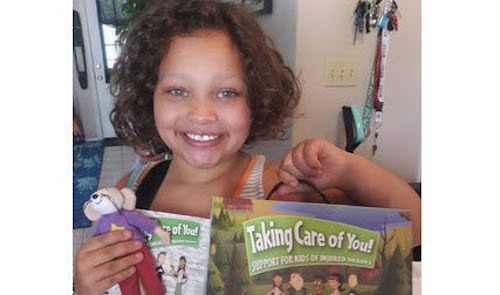 The child of a military veteran poses for a photo with her Comfort Kit provided by Comfort Crew, a community partner of WWP.