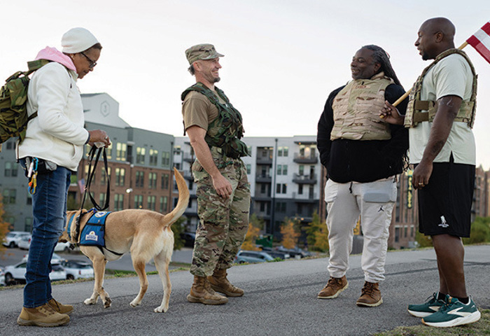 Warriors gather outdoors, connecting in conversation during a community event with a service dog nearby.