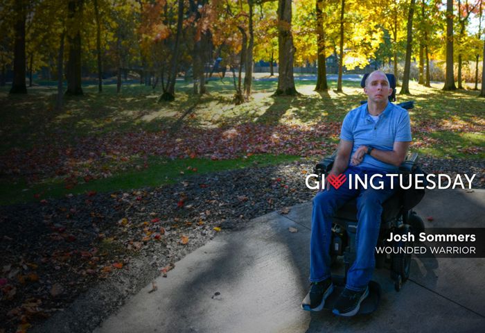 Wounded warrior Josh Sommers sits in his wheelchair in front of autumn leaves. He is looking at camera with serious face.