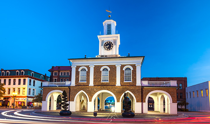 Market House in Fayetteville, NC with clock tower, light trails from cars, and clear blue sky during early morning or evening. 
