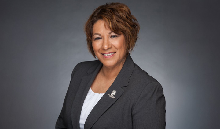 La cuidadora Cindy Parsons posa, sonriendo, con una chaqueta de traje gris que tiene un prendedor de Wounded Warrior Project en la solapa.