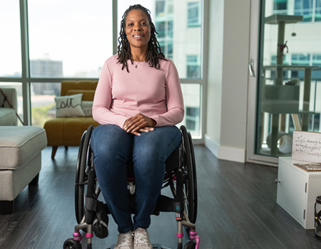 Sharona Young, a wounded warrior, sits in her wheelchair at home, smiling warmly at the camera.