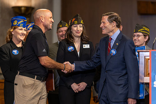 U.S. Army veteran Dan Nevins and Senator Richard Blumenthal shake hands in front of other people.