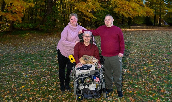 Wounded Warrior Angie Lupe sits in her wheelchair and smiles for a photo with her family outdoors. 