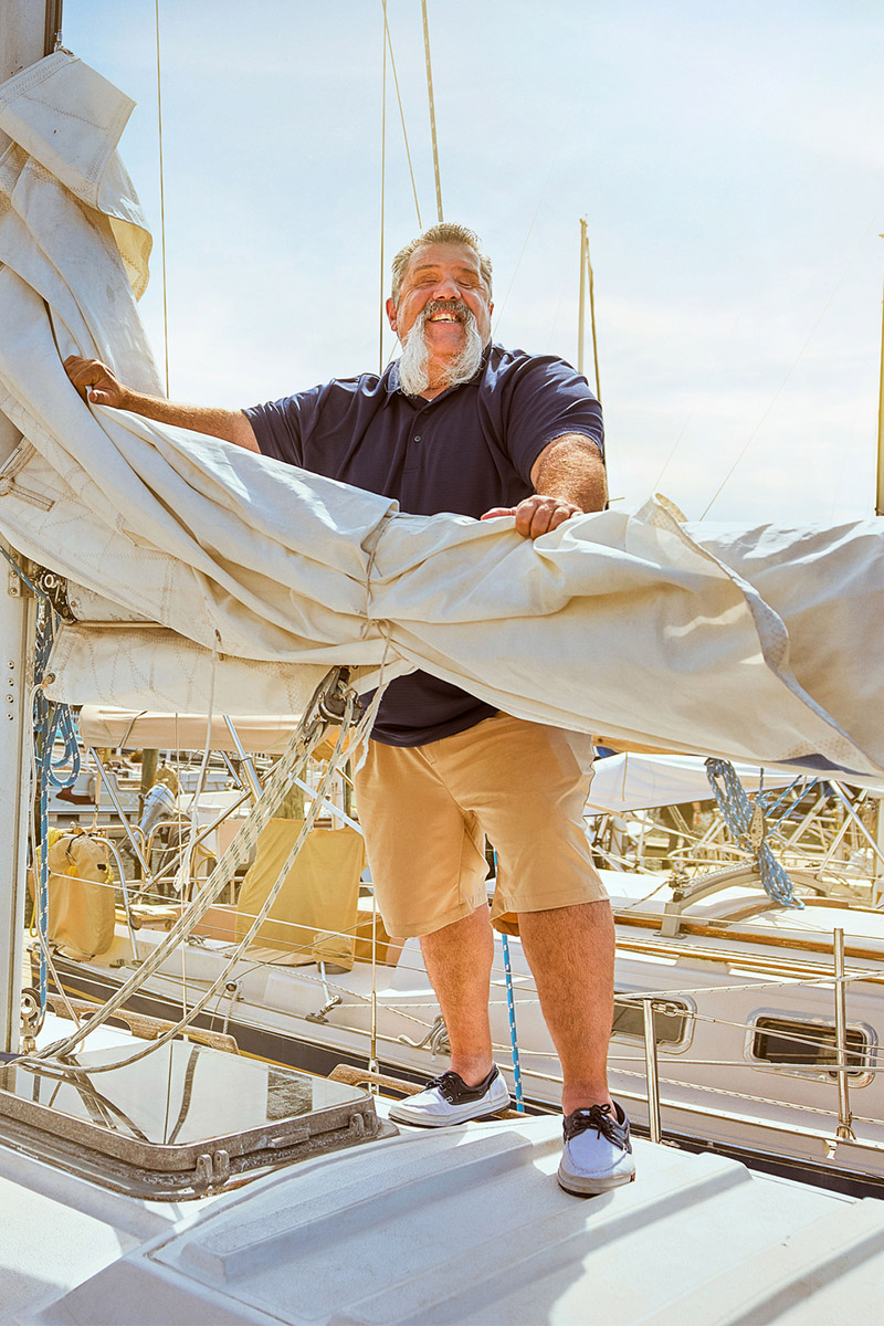 Wounded warrior Aaron Cornelius standing on a sailing yacht, holding the mast and smiling.