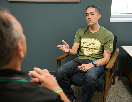 Warrior Sergio Alfaro speaks with a clinician while sitting in a chair.