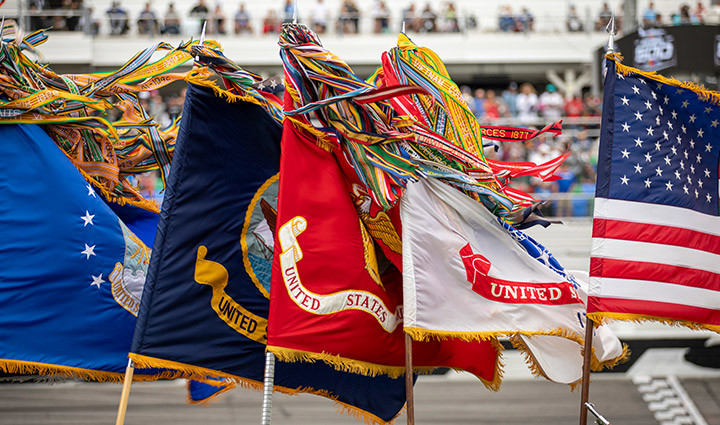 American and US military flags (Army, Marine, Navy, Air Force) are displayed outdoors, decorated with fringe and streamers.