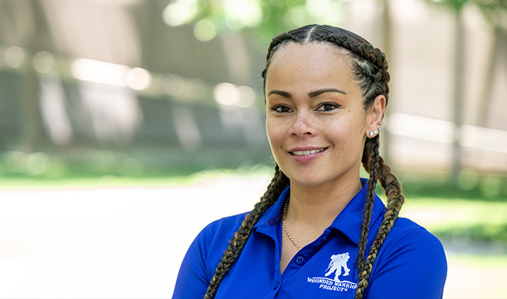 Antoinette Wallace, a wounded warrior, stands outside and smiles at the camera while wearing a blue WWP polo.