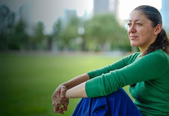 Warrior Ruth Corrigeux wears a green long sleeve shirt and jeans while sitting outside.