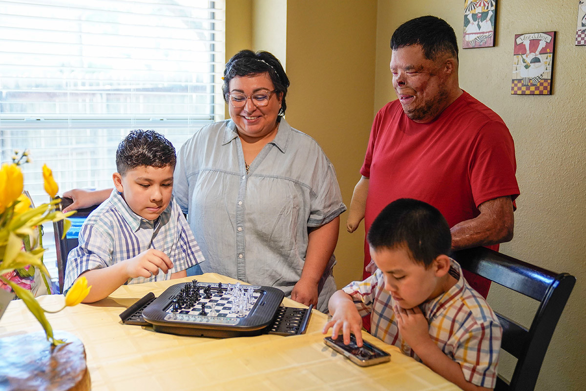 Wounded warrior Anthony Villareal and his wife smile as they watch their two boys play games at the family’s kitchen table.
