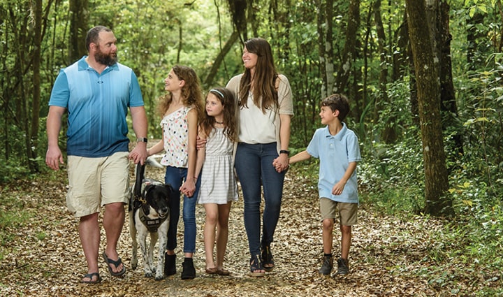 Wounded warrior Isaac Malone walking with his wife, Jenna, and their family in the woods with their dog.