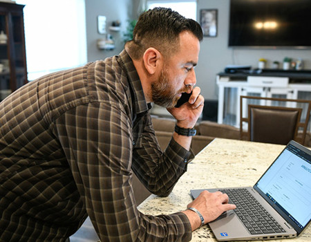 Wounded warrior Arnulfo Dauto reviews information on his computer while talking on the phone.