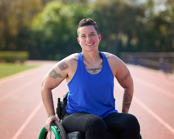 Beth King, veterana herida, en una silla de ruedas y sonriendo con una pista de fondo.