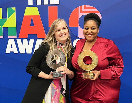 A female WWP employee holding a silver trophy stands smiling next to a female CSX executive holding a gold trophy in front of a sign that says Halo Awards.
