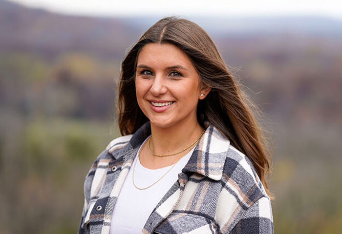 Wounded warrior Keara Torkelson smiling and wearing a plaid shirt standing in front of a scenic background.