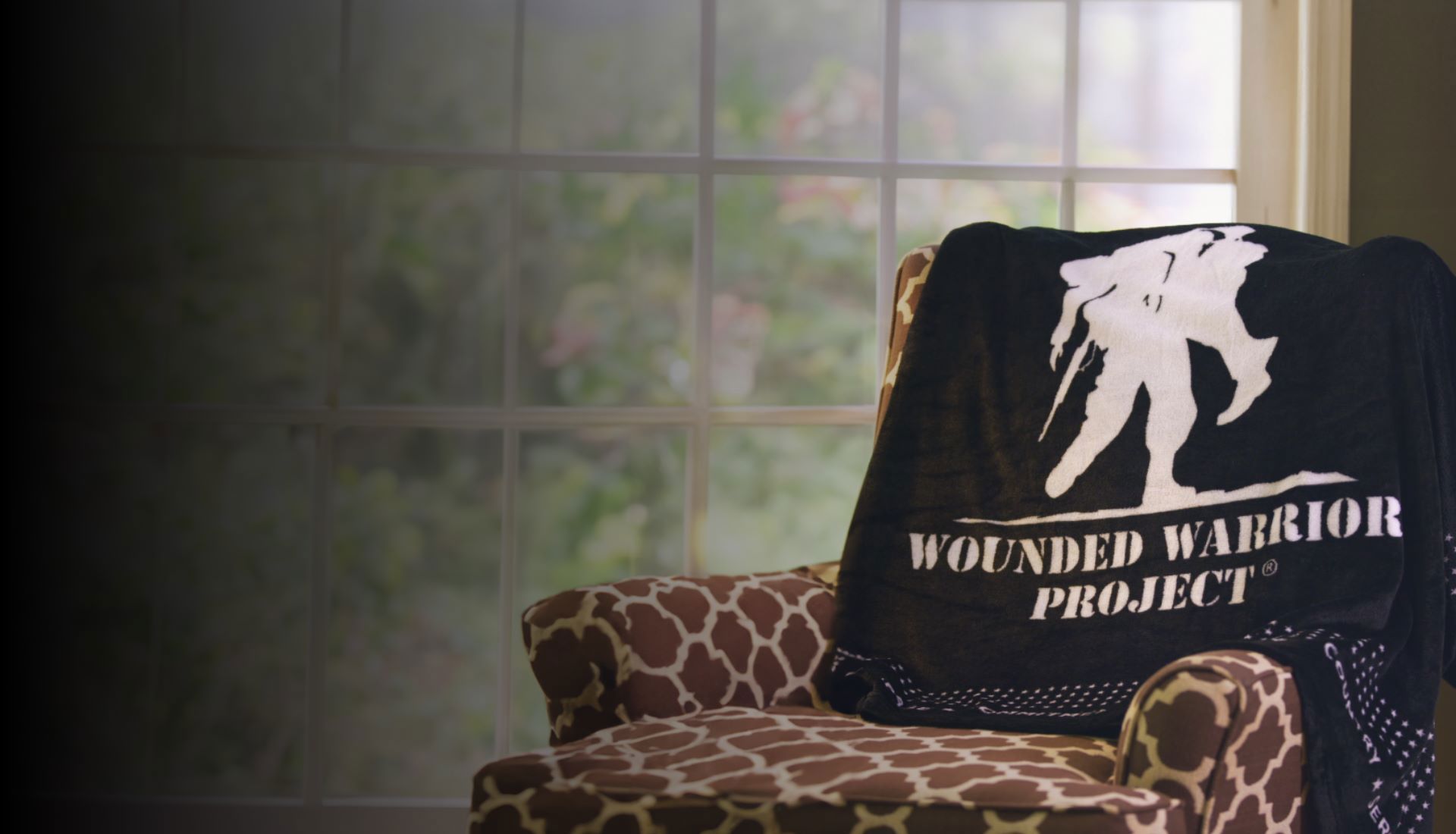A black fleece blanket featuring the Wounded Warrior Project® logo with a border of small stars is draped on an armchair.