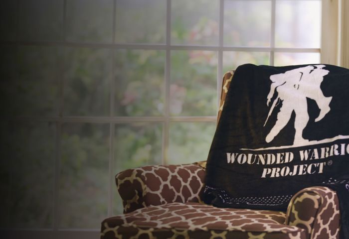 A black fleece blanket featuring the Wounded Warrior Project® logo with a border of small stars is draped on an armchair.