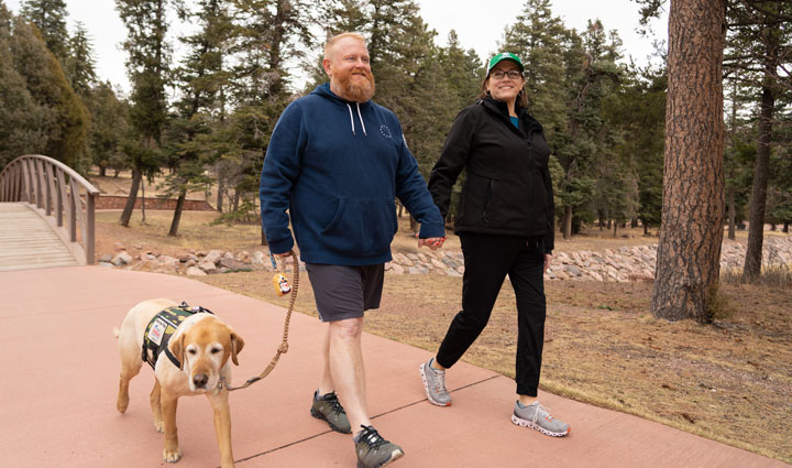 Wounded warrior Scott Highes and his wife Shea walk along a path with Scott's service dog.
