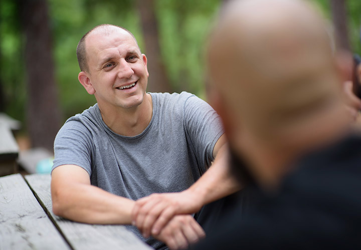 Wounded warrior James Rivera wears a grey t-shirt and smiles to another fellow warrior during a conversation. 