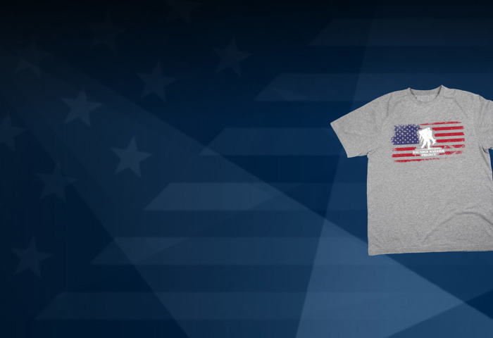A light gray shirt with the flag and the Wounded Warrior Project logo. Behind the T-shirt, a blue background of the American flag.