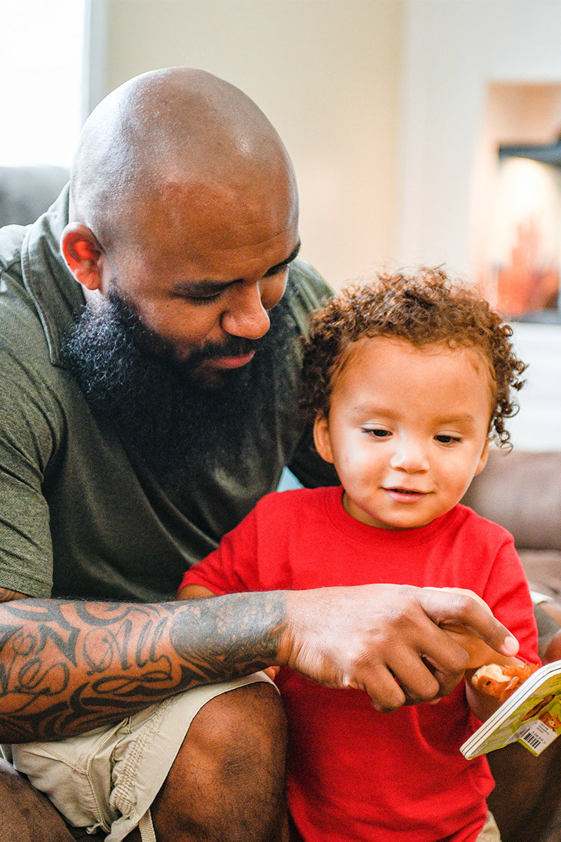 Wounded warrior Eric Delion peers over his toddler’s shoulder, pointing to a book while smiling and talking.