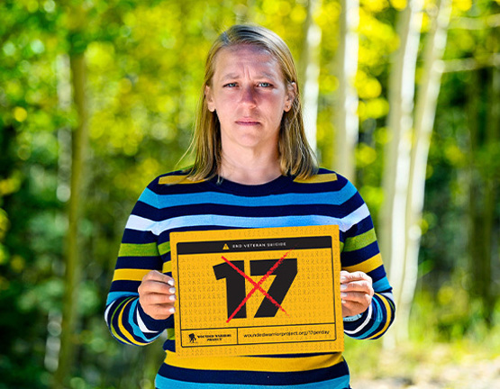 Warrior Angie Peacock wears a colorful shirt and holds a crossed-out 17 sign to support ending veteran suicide.