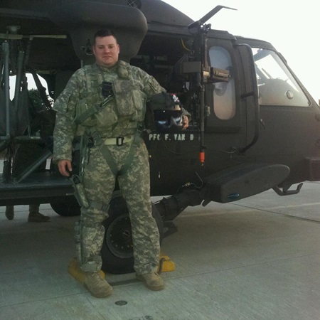 Jacob Norotsky in camouflage stands in front of a military helicopter, holding a helmet.