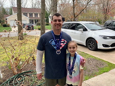 Byron and Kaylee stand outside, side by side, wearing matching Carry Forward 5K medals.