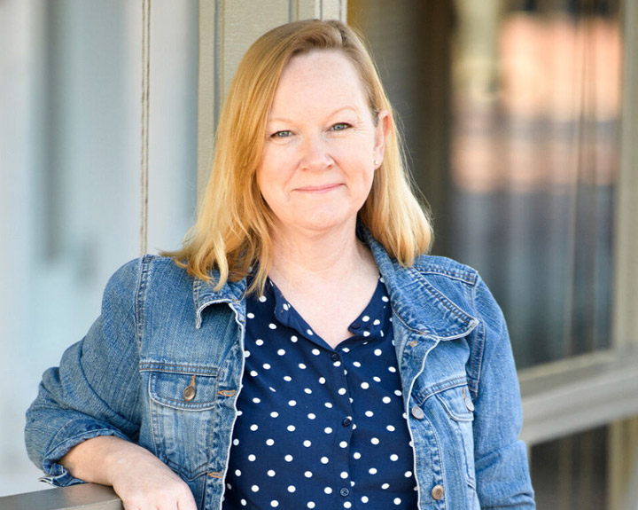 La cuidadora Jennifer Jenkins posa apoyada contra una baranda mientras sonríe.