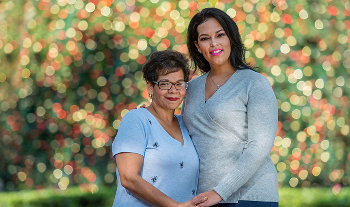 Warrior Yomari Cruz and her mother posing in front of a Christmas tree while holding hands.