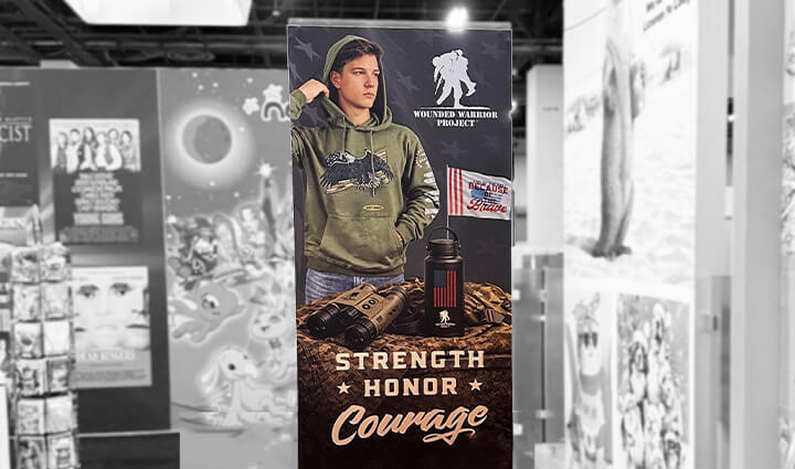 Tradeshow banner displaying Wounded Warrior Project logo, person in green hoodie, branded products, and Strength • Honor • Courage.