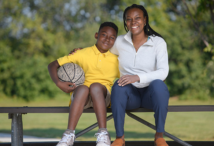 Warrior, Danielle Green sitting in a park with her son holding a basketball with her prosthetic hand.