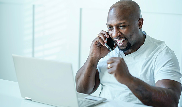 El veterano Melvin Gatewood sonríe y levanta el brazo izquierdo con emoción, mirando su ordenador con el móvil en la oreja derecha.