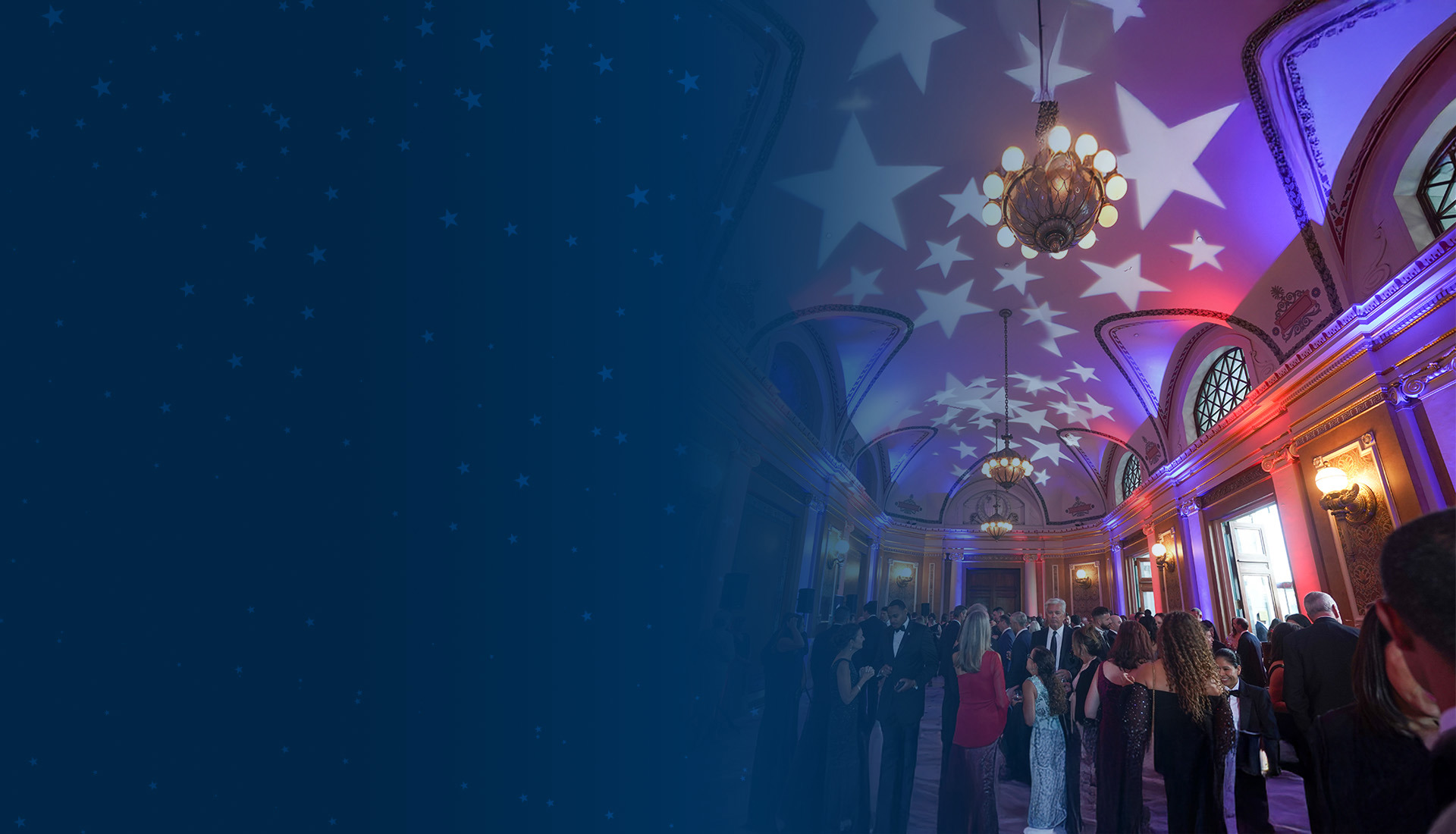 A grand ballroom with the celling illuminated with red, white, and blue lights projecting star shapes. The room is filled with people dressed in formal attire, engaging in conversation and socializing for WWP's Courage Awards and Benefit Dinner.