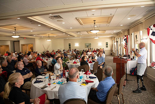 Audience seated in a ballroom listening to a wounded warrior speaking at the front.