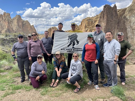Group outside in front of desert mountain holding a Wounded Warrior Project flag