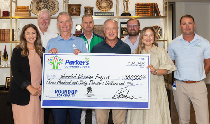 El director ejecutivo de WWP, Walt Piatt, y el ejecutivo de Parker's Kitchen Greg Parker sostienen un gran cheque de donación rodeados de personal masculino y femenino.